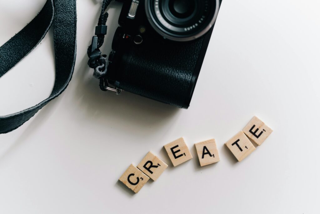 Camera resting next to Scrabble tiles spelling 'CREATE' on a white background.